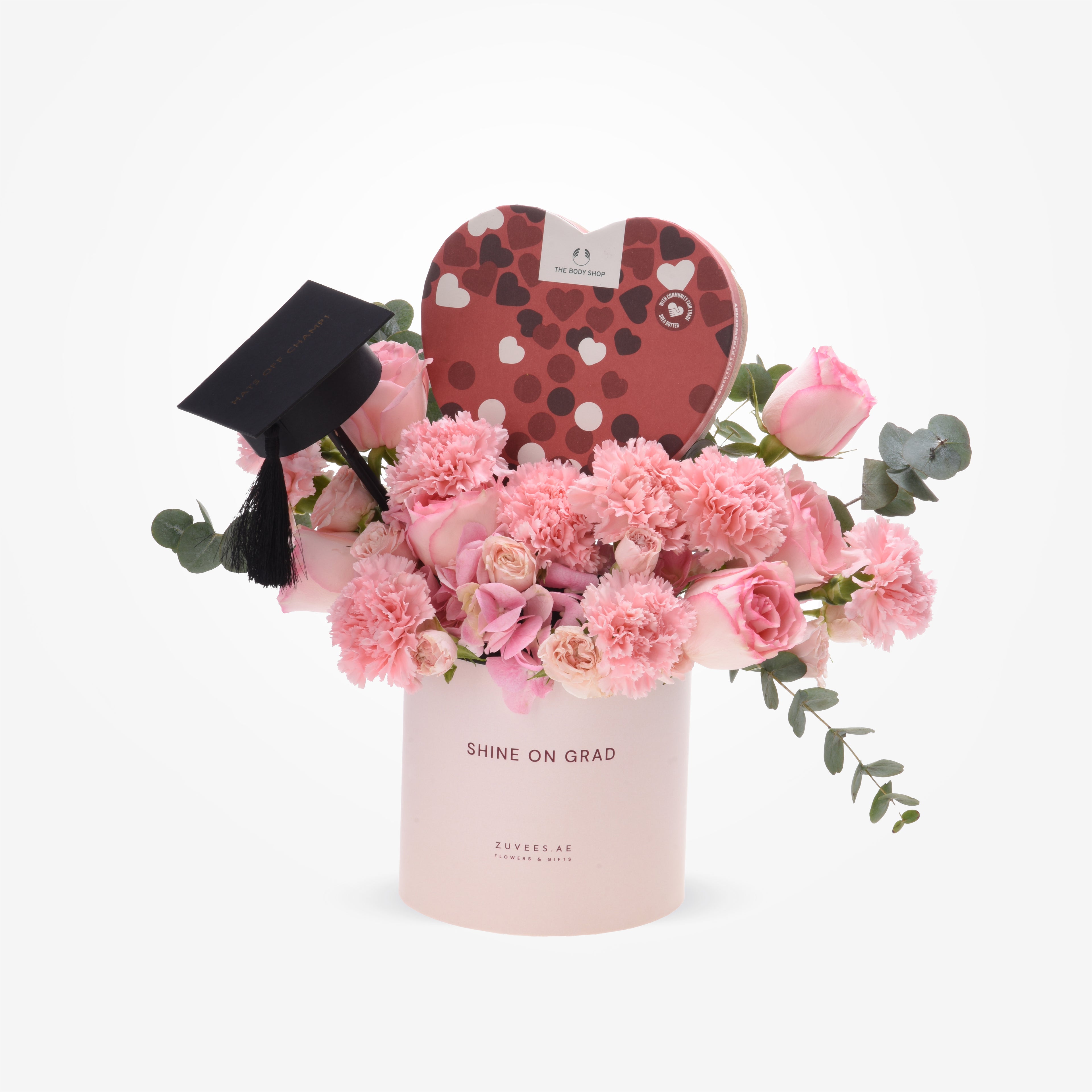 Pink roses, carnations, eucalyptus, graduation cap, heart-shaped Body Shop gift in "Shine On Grad" box.