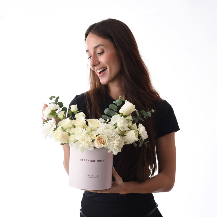 Woman smiles holding elegant white rose bouquet in pink "Happy Birthday" box.