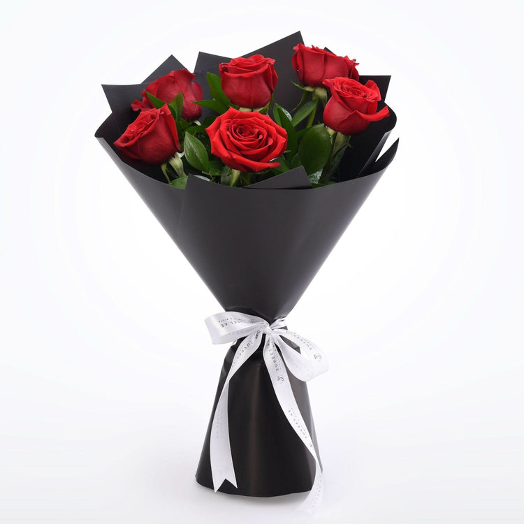 Vibrant red roses in sleek black paper, accented with elegant white ribbon.