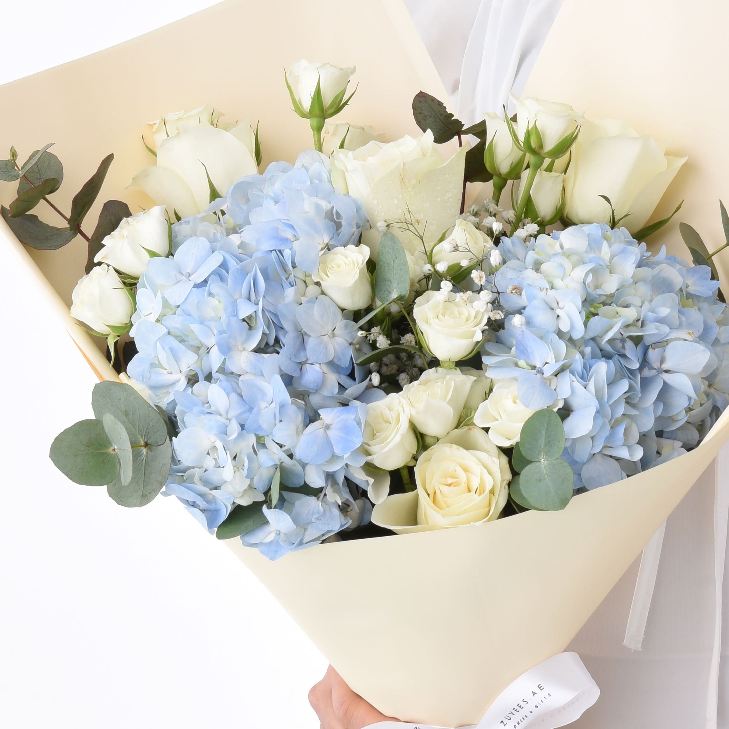Elegant white roses and soft blue hydrangeas wrapped in cream paper, accented with eucalyptus.