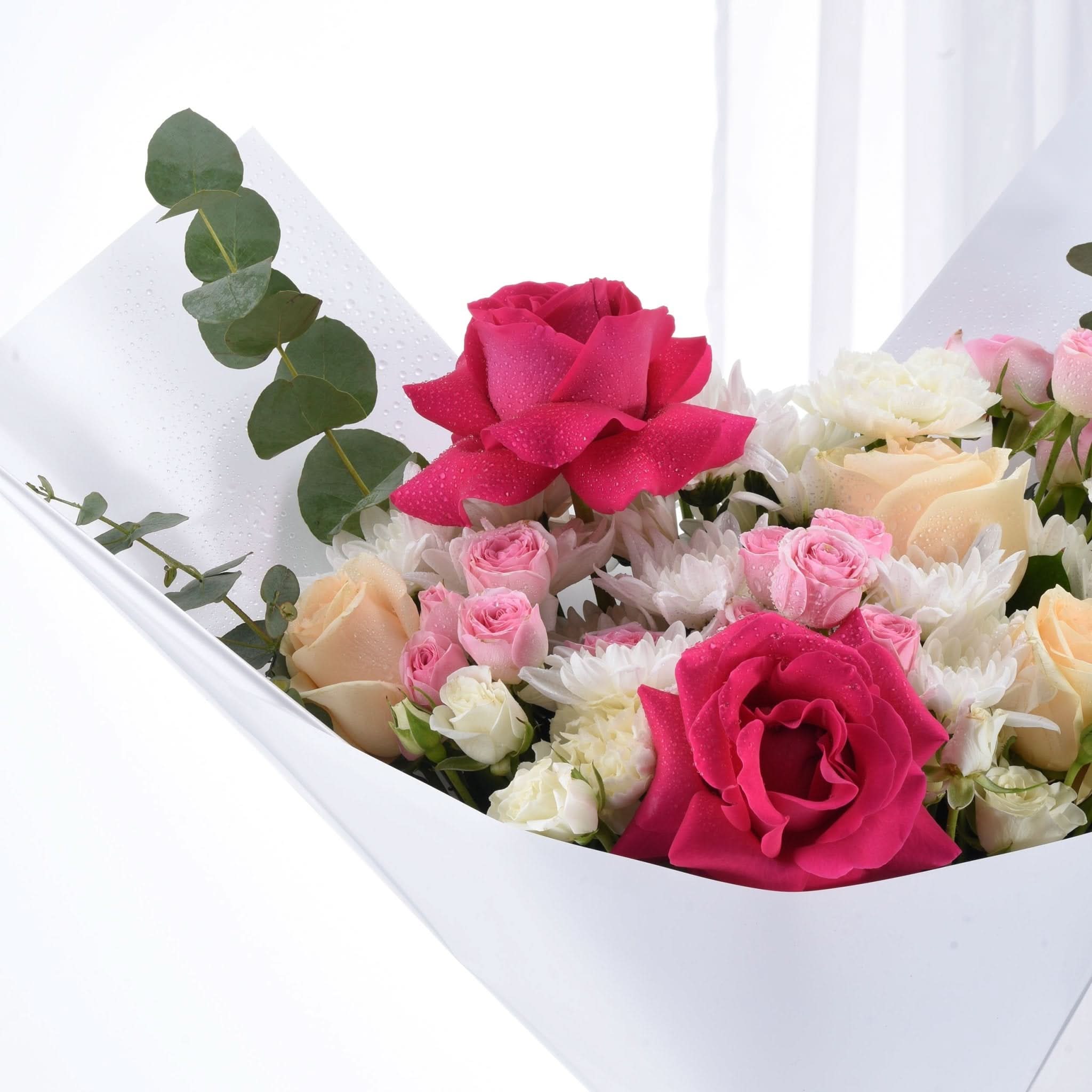 Vibrant pink, peach, and white roses with eucalyptus in dew-kissed white box bouquet.