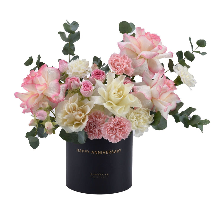 Elegant pink and cream roses, carnations, and eucalyptus in black "Happy Anniversary" box.