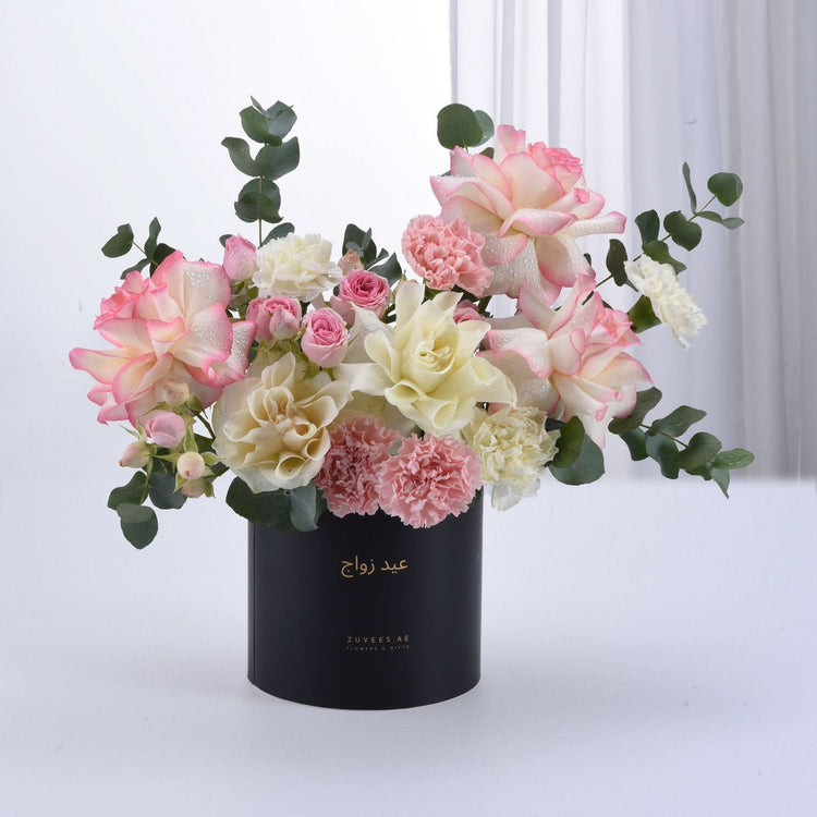 Elegant pink and cream roses, carnations, and eucalyptus in sleek black cylindrical vase.
