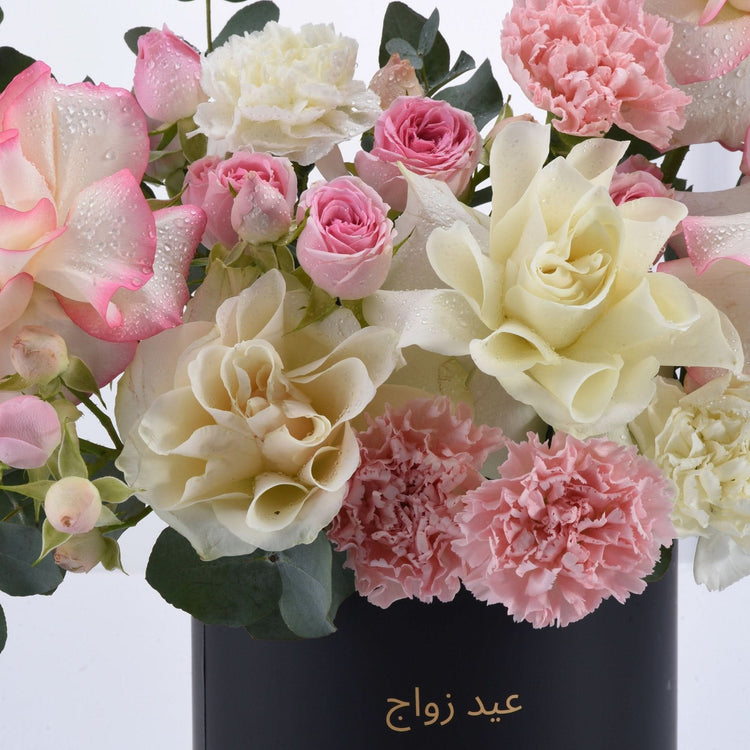 Soft pink and cream roses, carnations, dewdrops, elegant black vase with gold Arabic script.