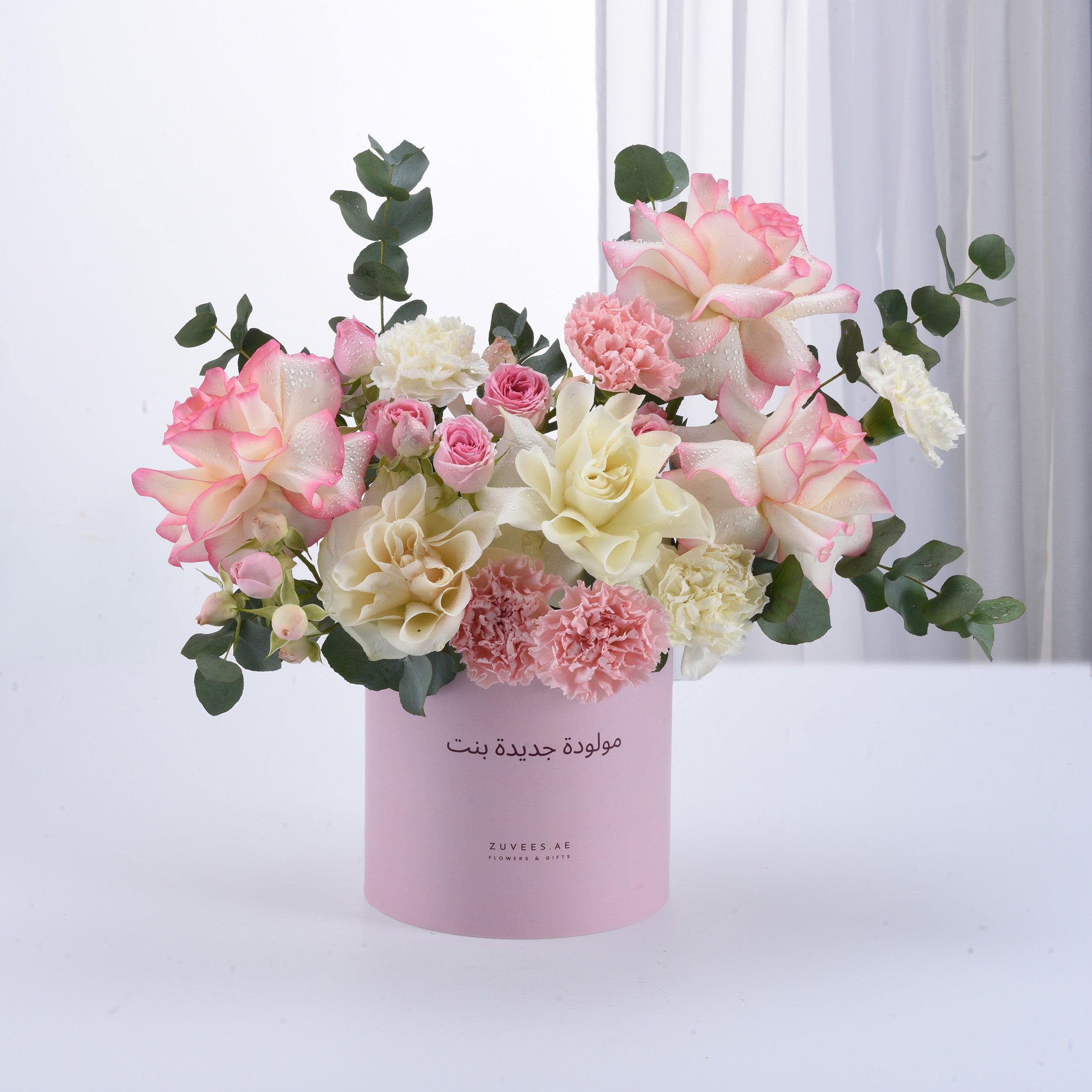 Soft pink and white roses, carnations, and eucalyptus in pastel pink cylinder vase.