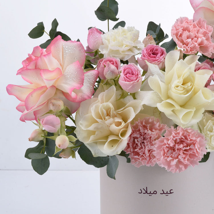 Pink and cream roses with carnations, dew-kissed petals, green eucalyptus, elegant white vase, Arabic text.