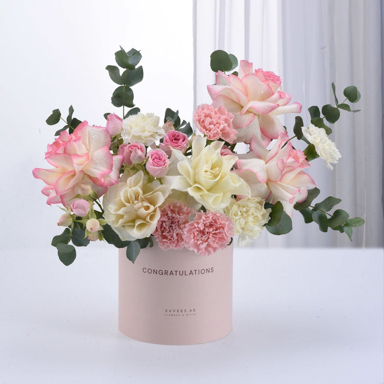 Pastel pink and cream roses, carnations, and eucalyptus in a "Congratulations" box.