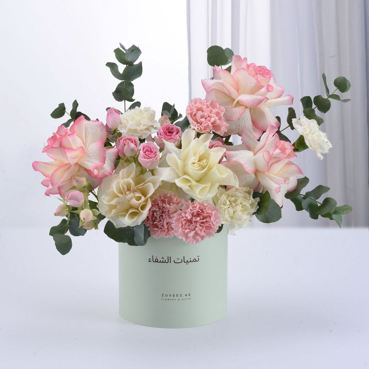 Pastel pink, cream roses and carnations in mint-green box with Arabic text.