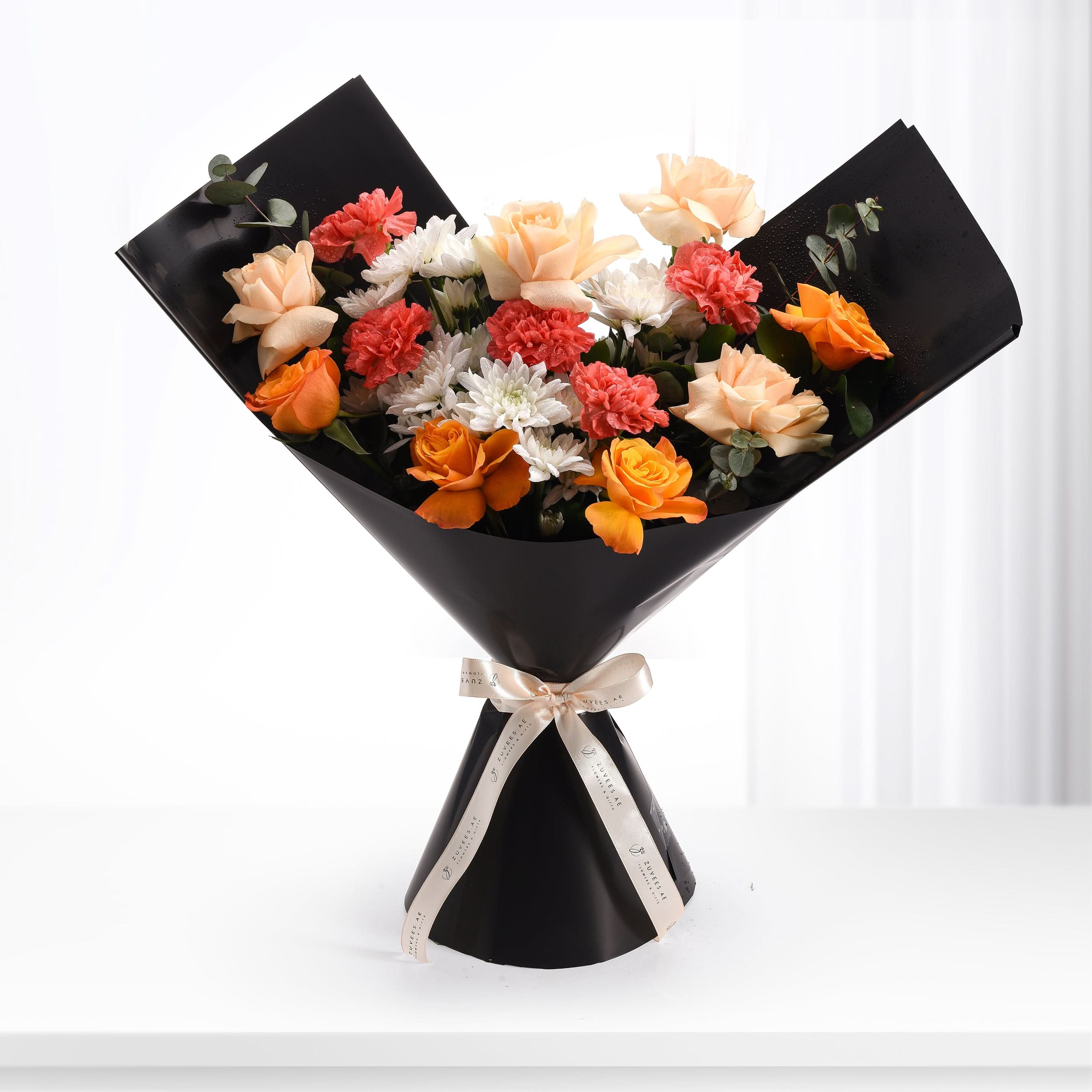 Vibrant orange, peach, coral, and white blooms elegantly wrapped in sleek black paper with gold ribbon.
