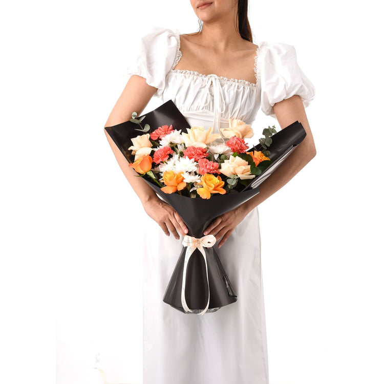 Black-wrapped bouquet with roses, carnations, and eucalyptus, tied with cream ribbon.