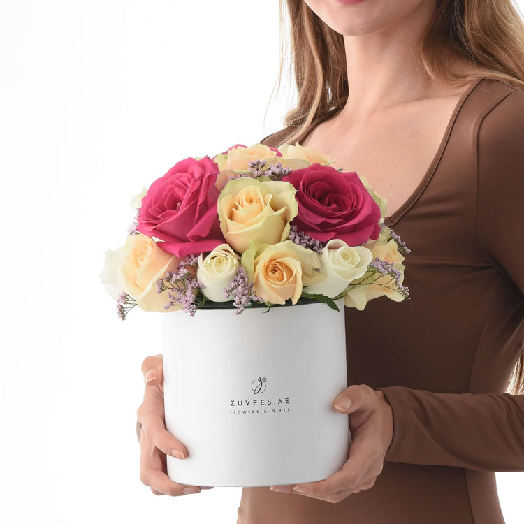Woman holds elegant white hat box filled with vibrant pink, yellow, and cream roses.