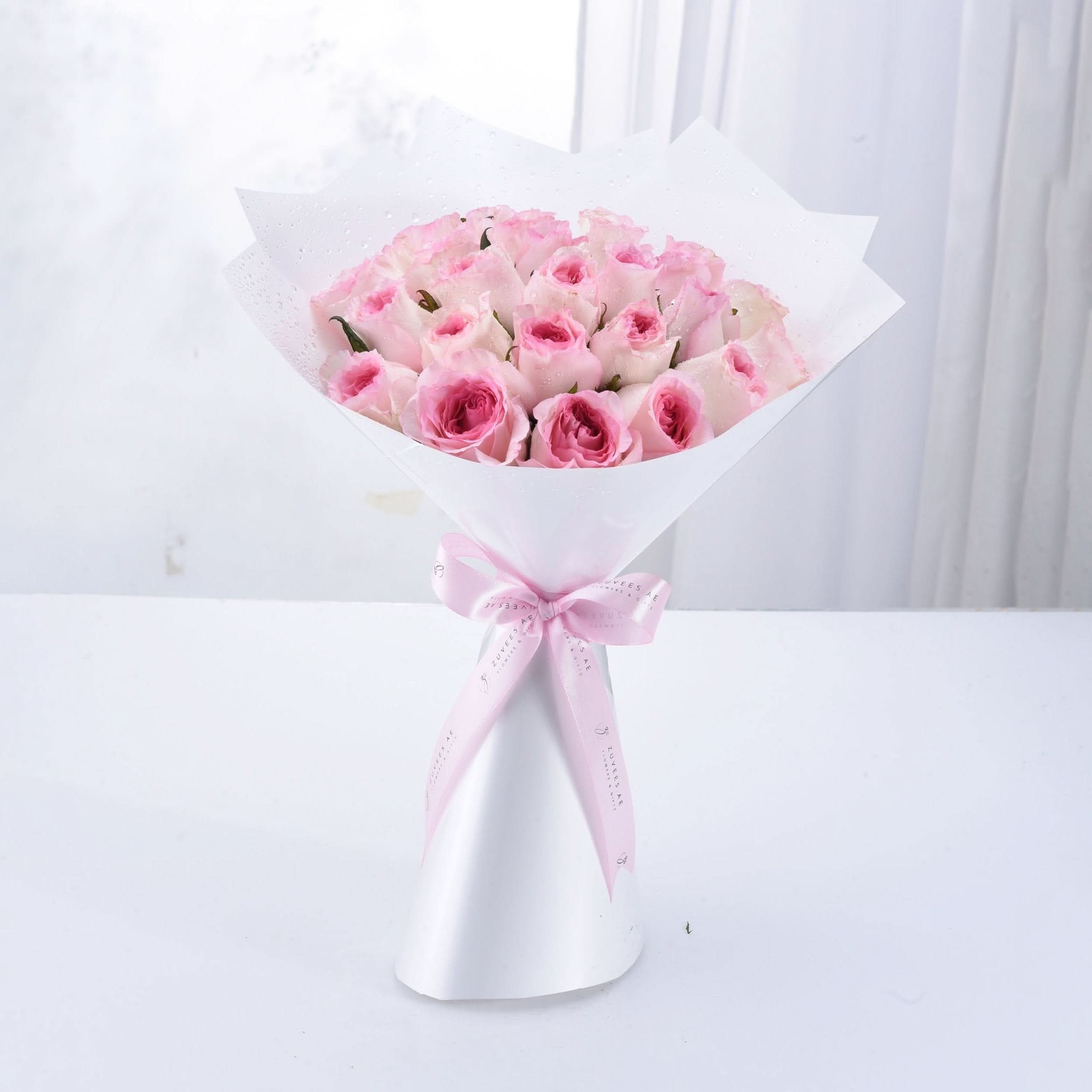 Soft pink roses in white paper, tied with pink ribbon bow.
