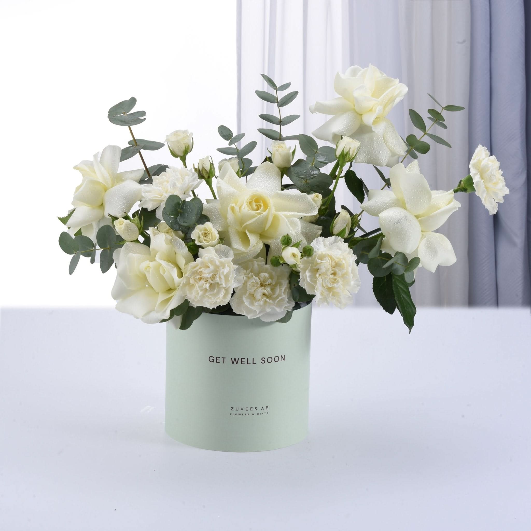 White roses, carnations, eucalyptus in mint "Get Well Soon" box, dew-kissed, elegant gift.