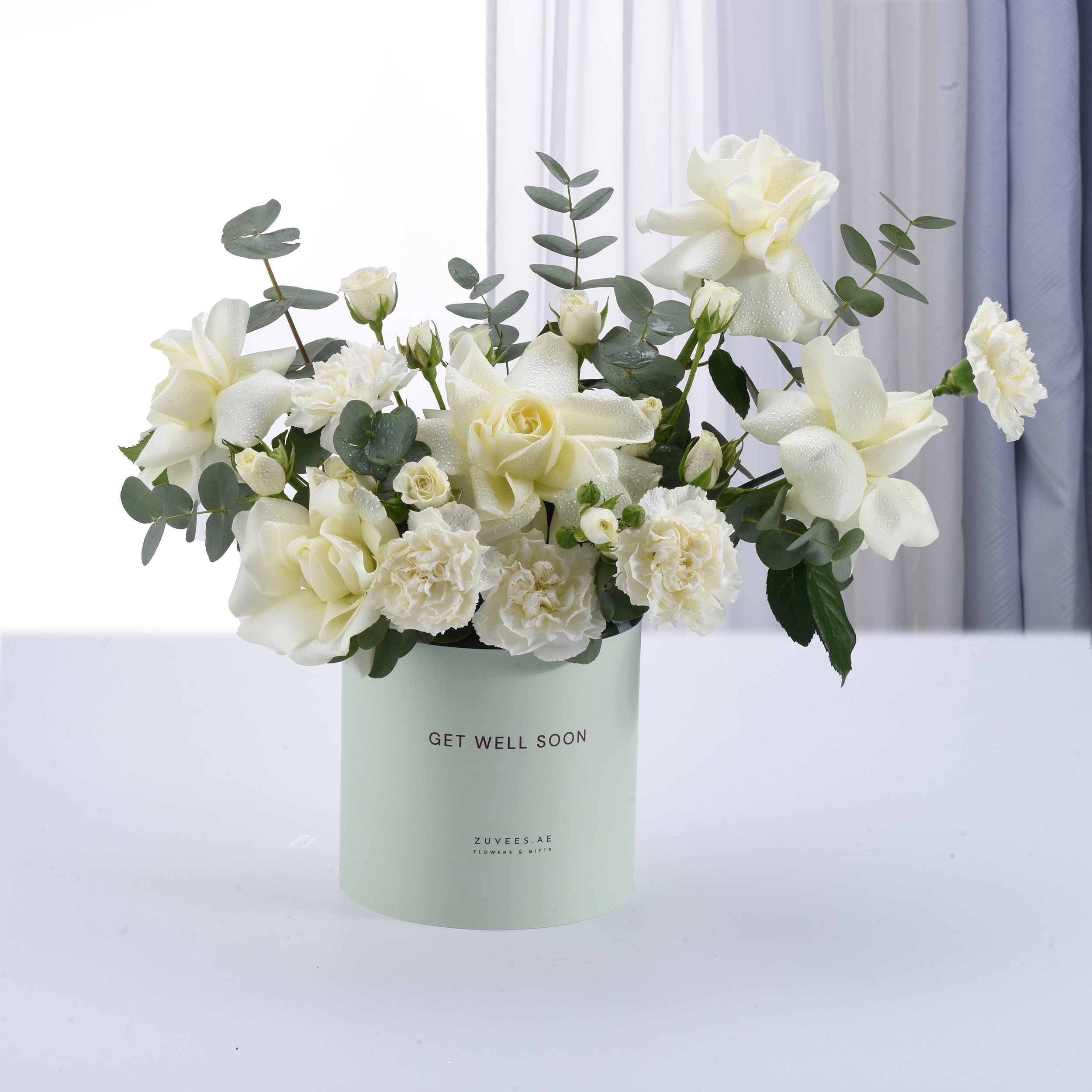 White roses, carnations, eucalyptus in mint "Get Well Soon" box, dew-kissed, elegant sympathy gift.