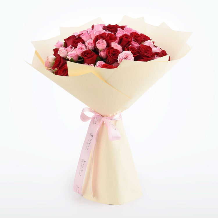 Vibrant red and pink roses wrapped in cream paper with pink ribbon.