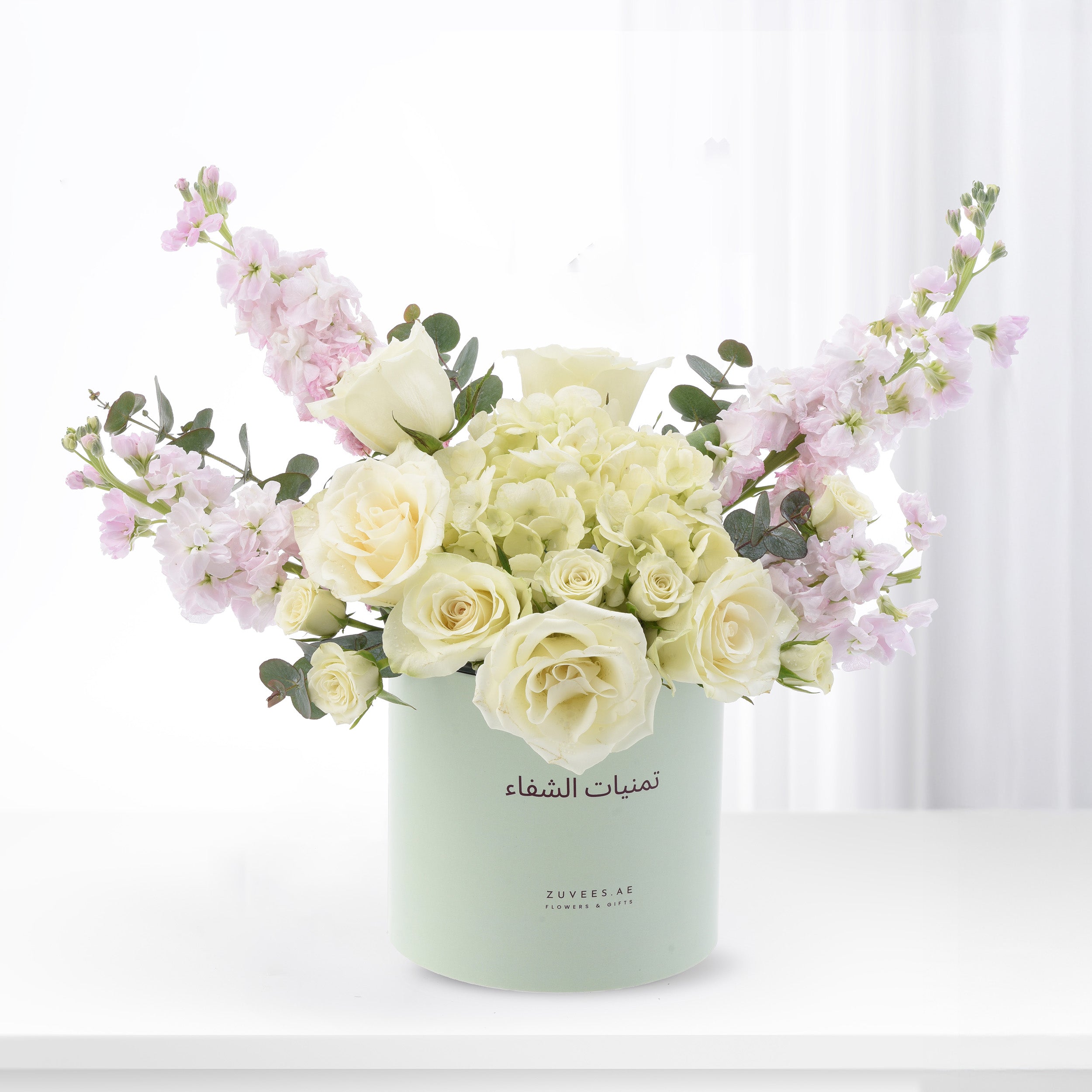 Elegant white roses, pink stock, and hydrangeas in mint green Zuvees box, soft light, luxury floral gift.