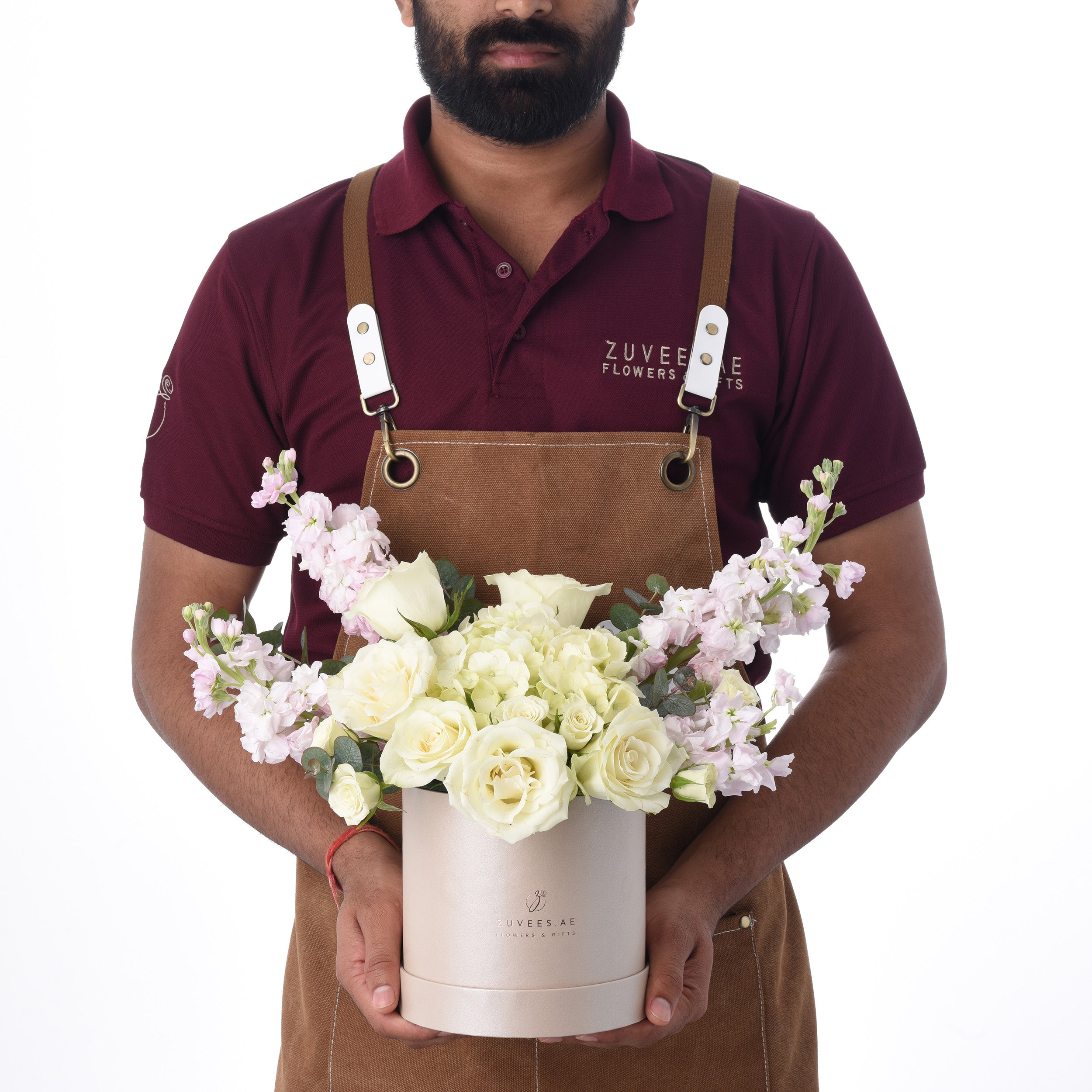 Floral arranger presents elegant white rose bouquet in branded rose-gold box.