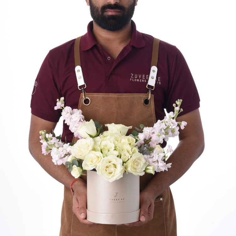 Floral arranger presents elegant white rose bouquet in branded rose-gold box.