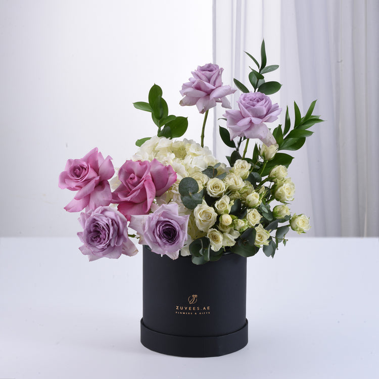 Elegant lavender, pink, and white roses in sleek black box with greenery.