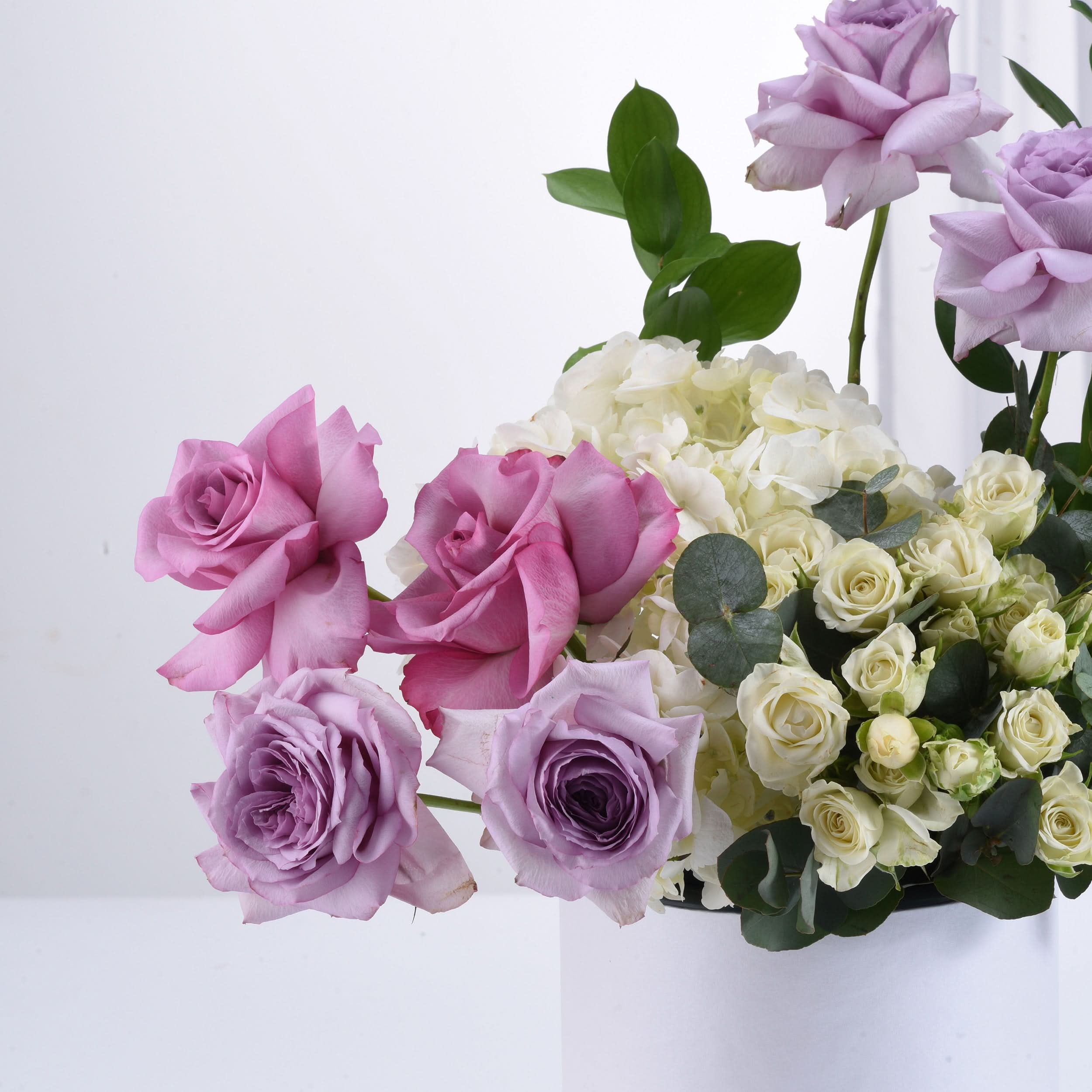 Lavender, pink, and white roses with hydrangeas and eucalyptus in elegant floral arrangement.