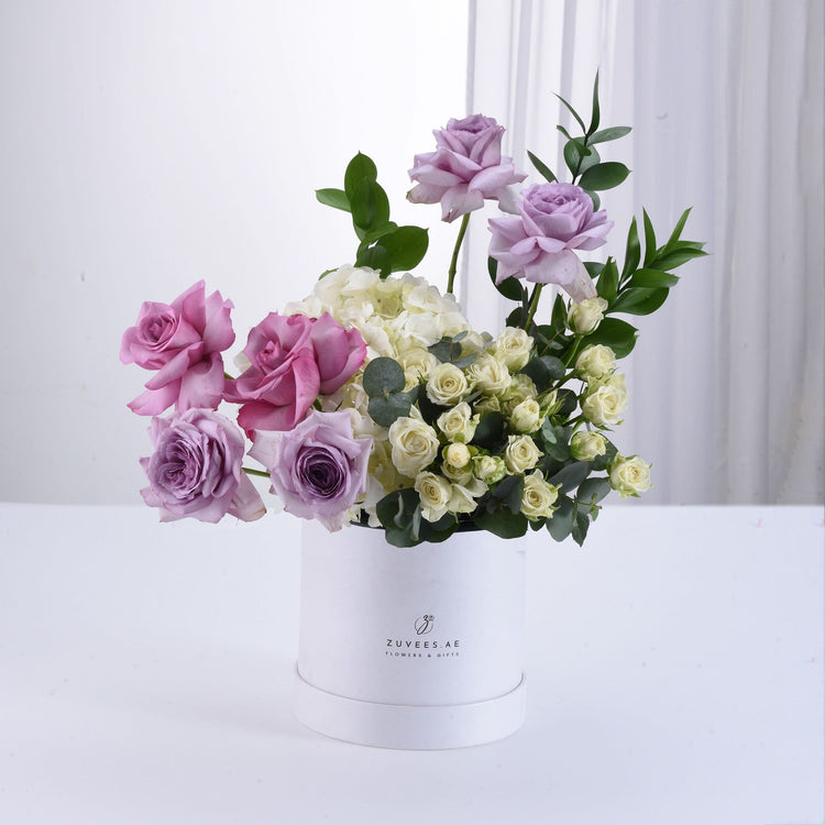 Elegant lavender, pink, and cream roses in white cylindrical box.