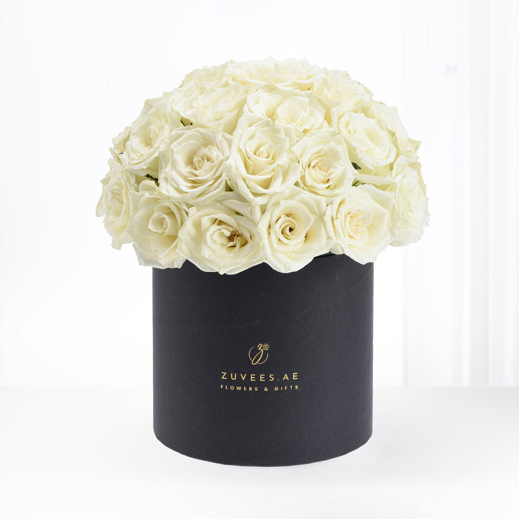 Luxurious cream roses overflowing from matte black box with gold branding.