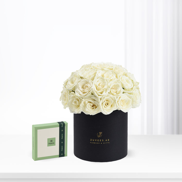 Elegant ivory roses in matte black hat box beside green Patchi gift box.