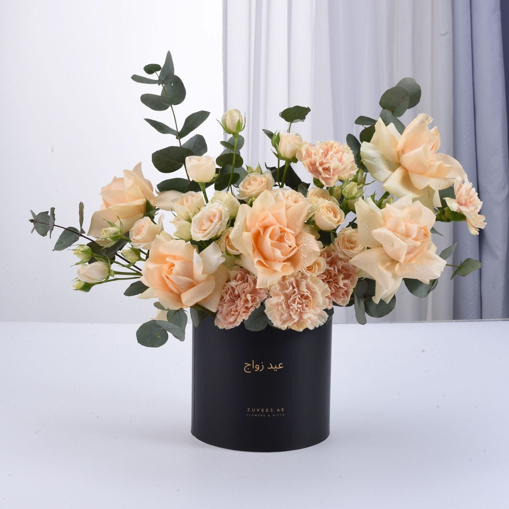 Elegant peach roses and carnations in sleek black vase with gold script.