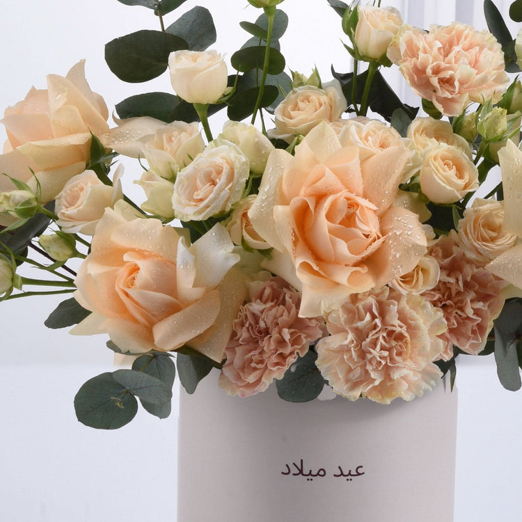 Soft peach roses and carnations in white vase with Arabic birthday text.
