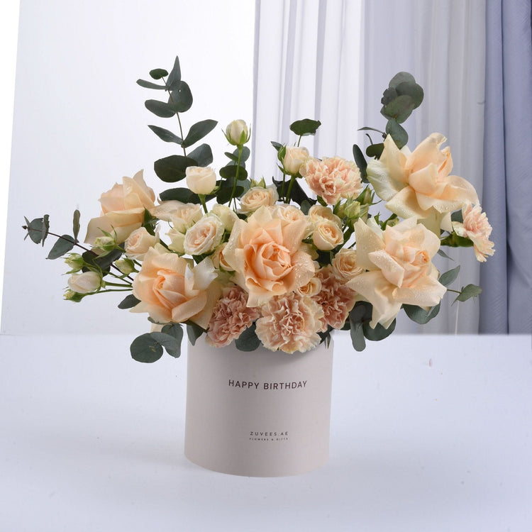 Elegant peach roses, carnations, eucalyptus in "Happy Birthday" box, soft pastel tones, dew-kissed petals.