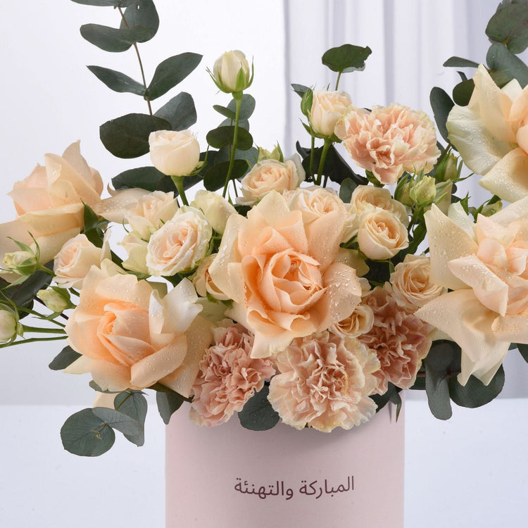 Soft peach roses and carnations in pink vase with Arabic “Congratulations” text.