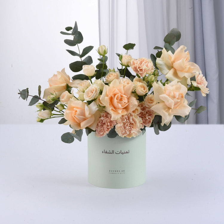 Pastel peach roses and carnations in mint cylinder vase with Arabic text.