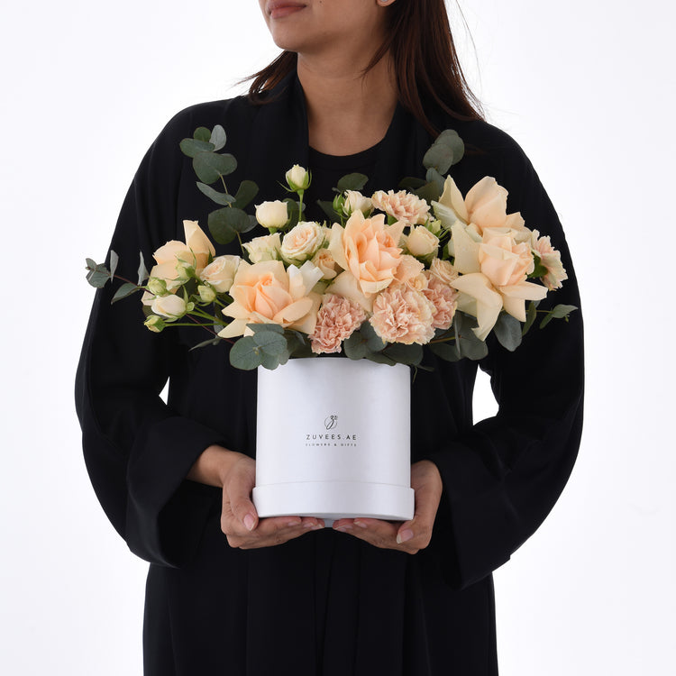 Elegant peach roses and carnations in sleek white box held by woman in black.