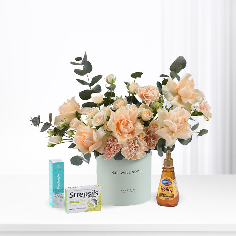 Pastel peach roses and eucalyptus in mint vase with honey, throat lozenges, and electrolyte for recovery.
