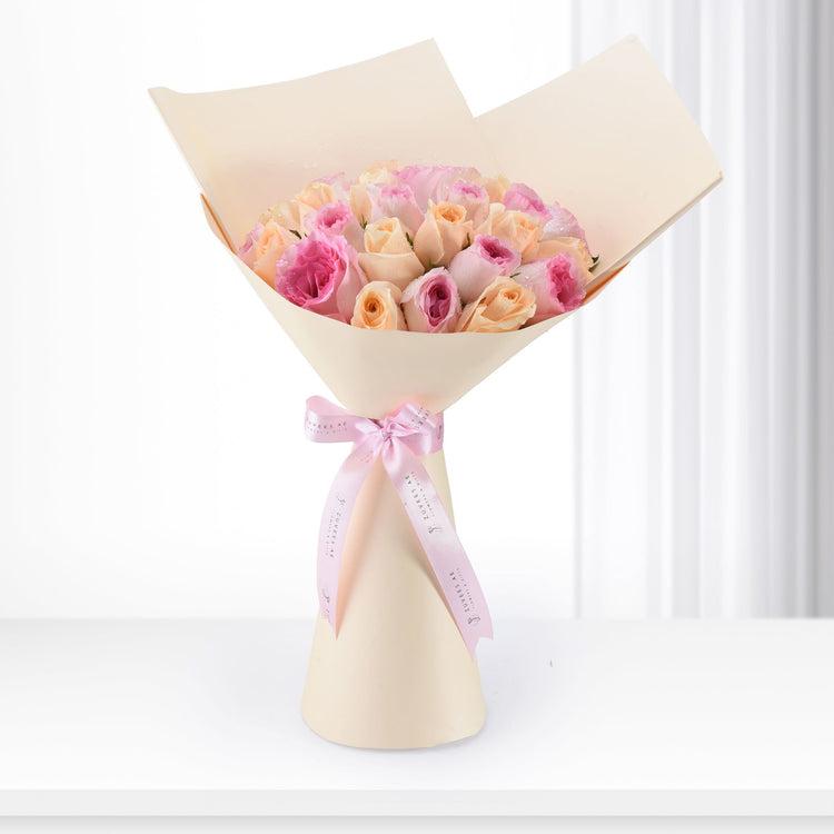 Delicate pink and peach roses wrapped in cream paper, tied with branded ribbon, perfect for gifting.