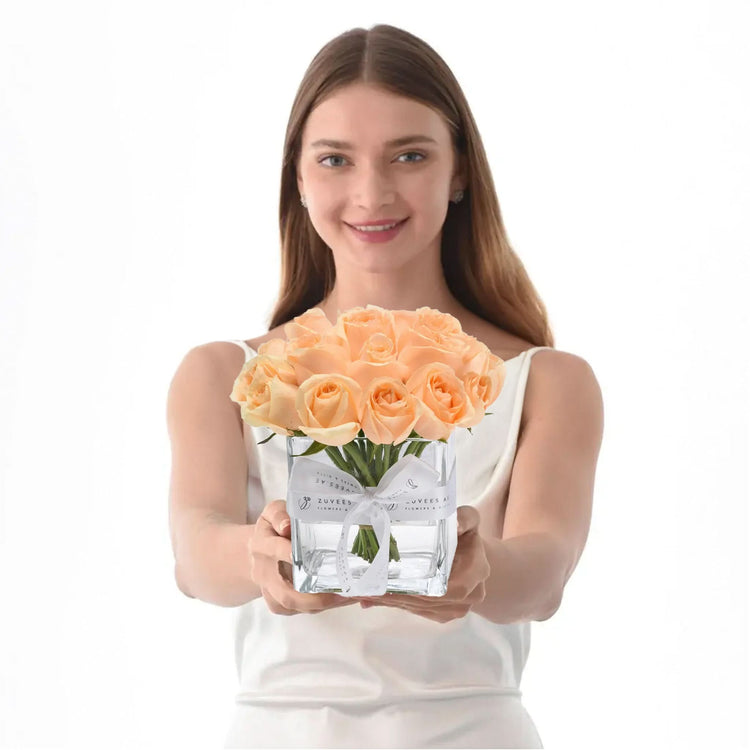 Woman presents peach roses in clear glass vase with white ribbon.