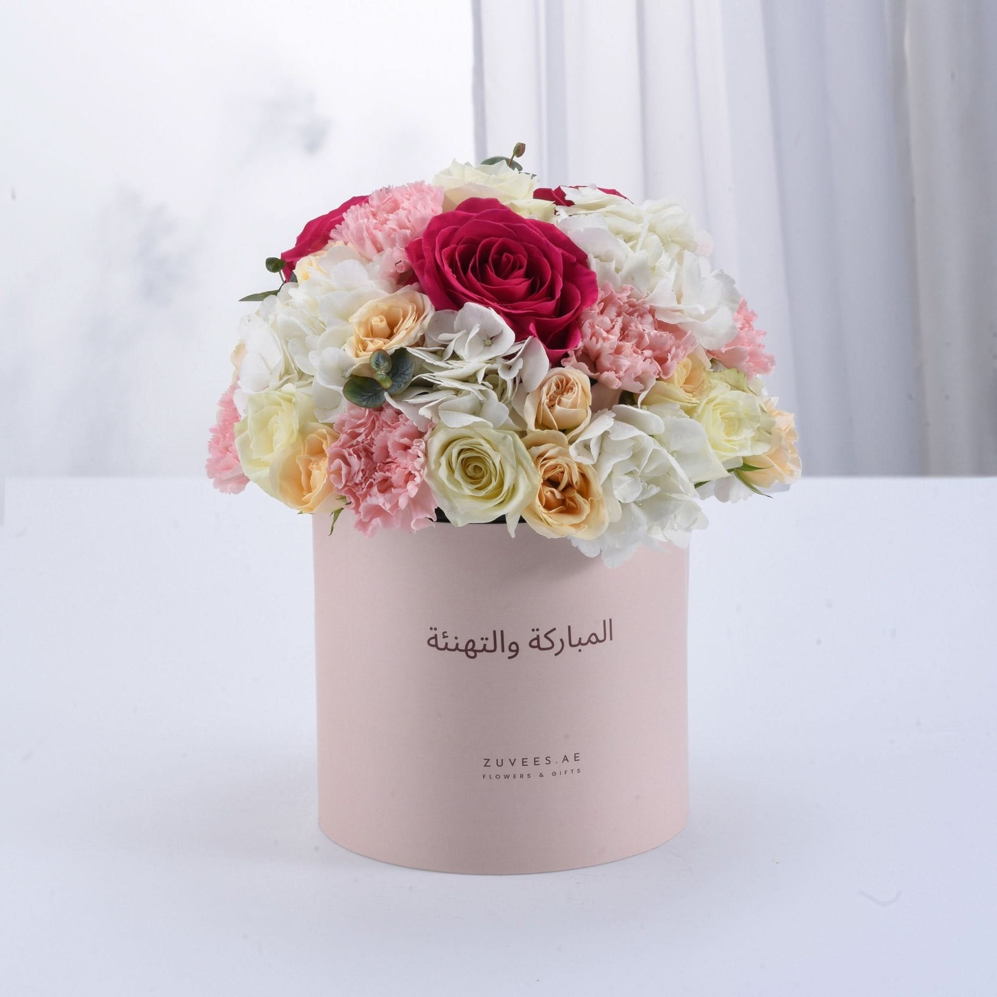 Soft pink box holds vibrant roses, hydrangeas, and carnations for elegant celebration.