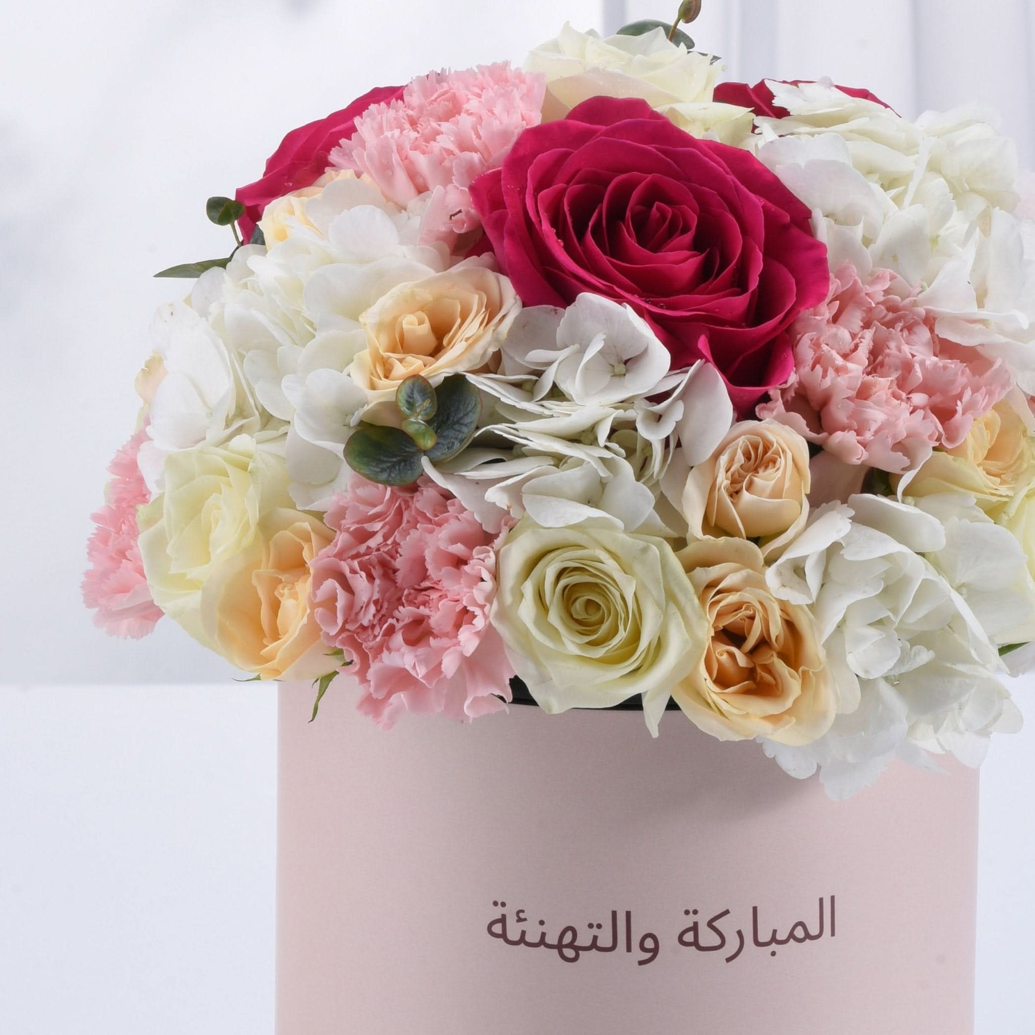 Pink box holds vibrant roses, carnations, and hydrangeas; Arabic text reads "Congratulations and Happy Birthday."