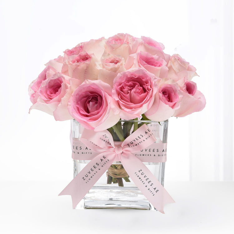 Soft pink roses in clear glass vase, elegantly tied with branded ribbon.