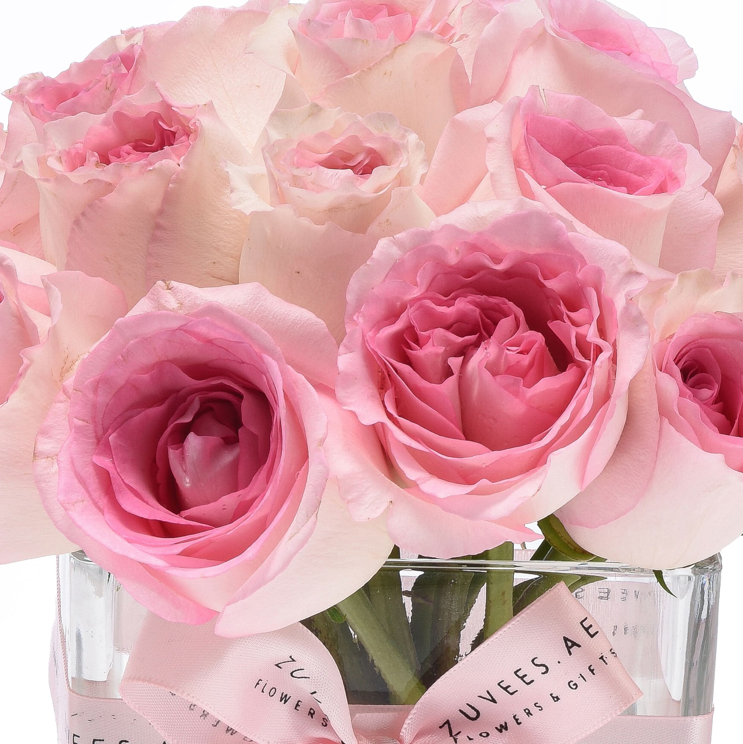 Soft pink roses in clear vase, elegantly wrapped with branded ribbon.