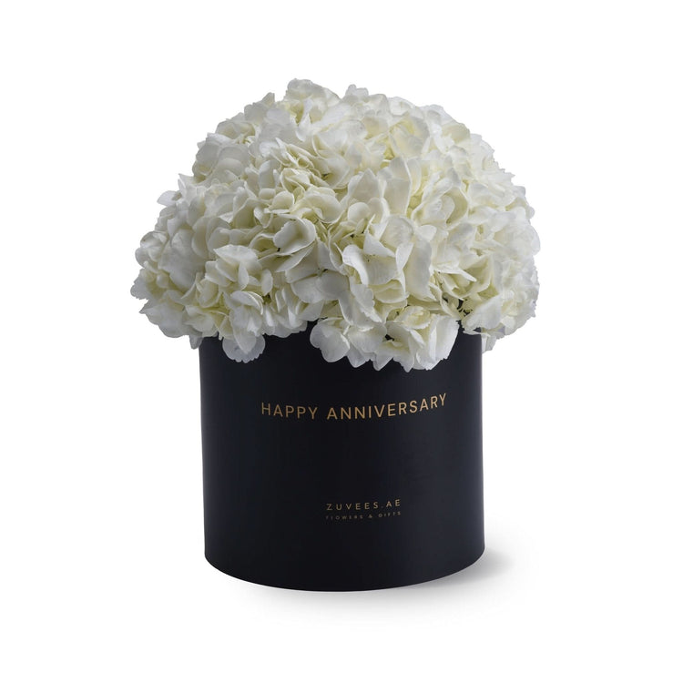 Elegant white hydrangeas in black "Happy Anniversary" gift box, gold lettering, minimalist luxury floral arrangement.
