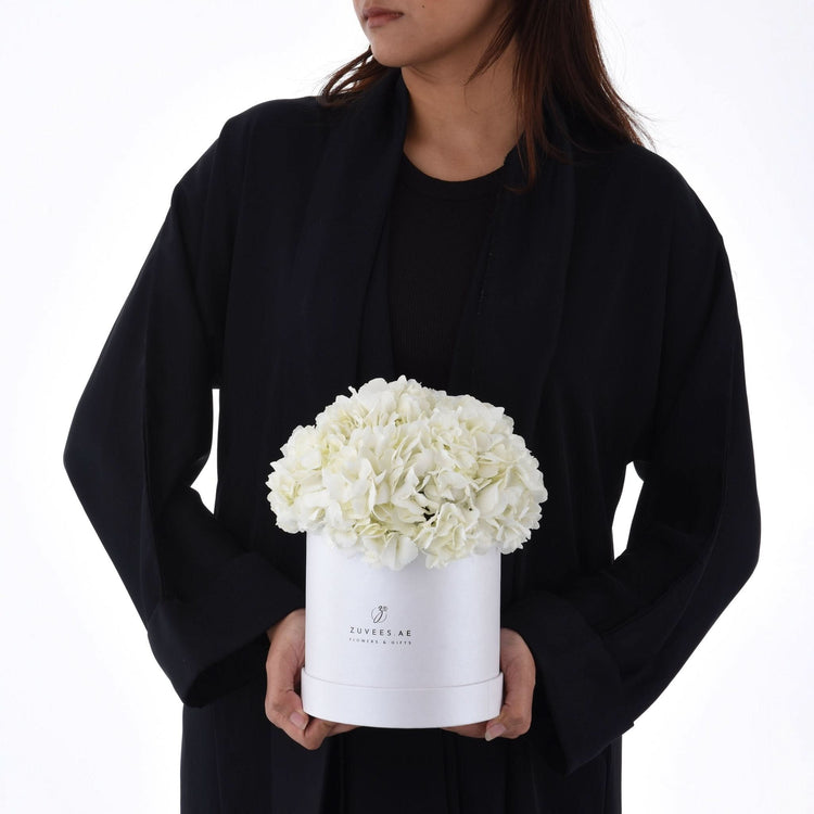 White hydrangeas in sleek white box, held by person in black, minimalist luxury floral gift.