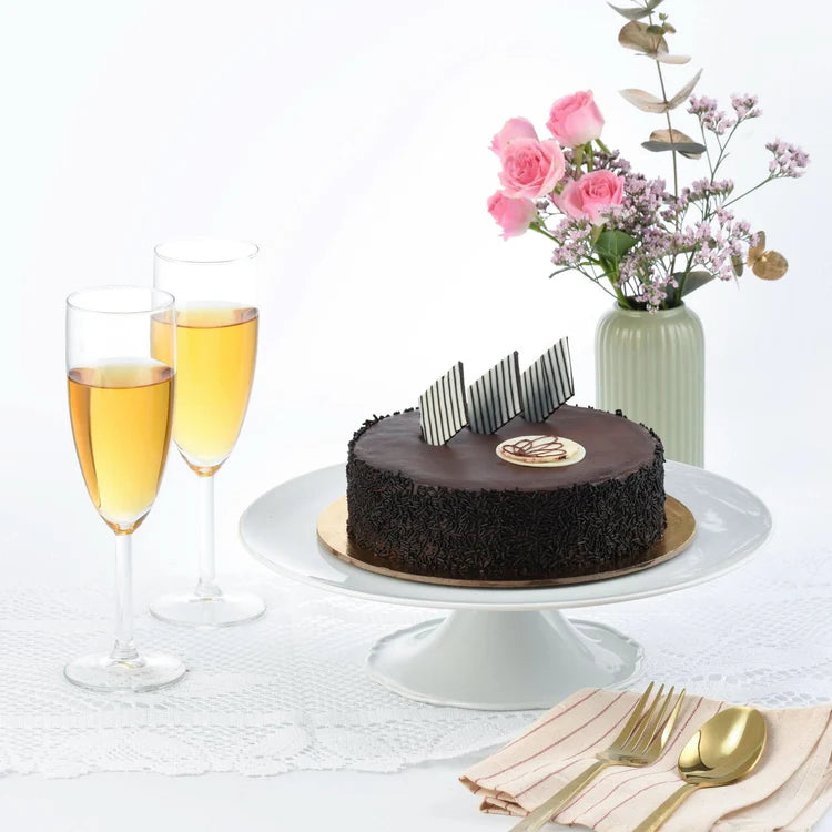 Rich chocolate cake with striped topper, champagne flutes, pink floral vase, elegant table setting.