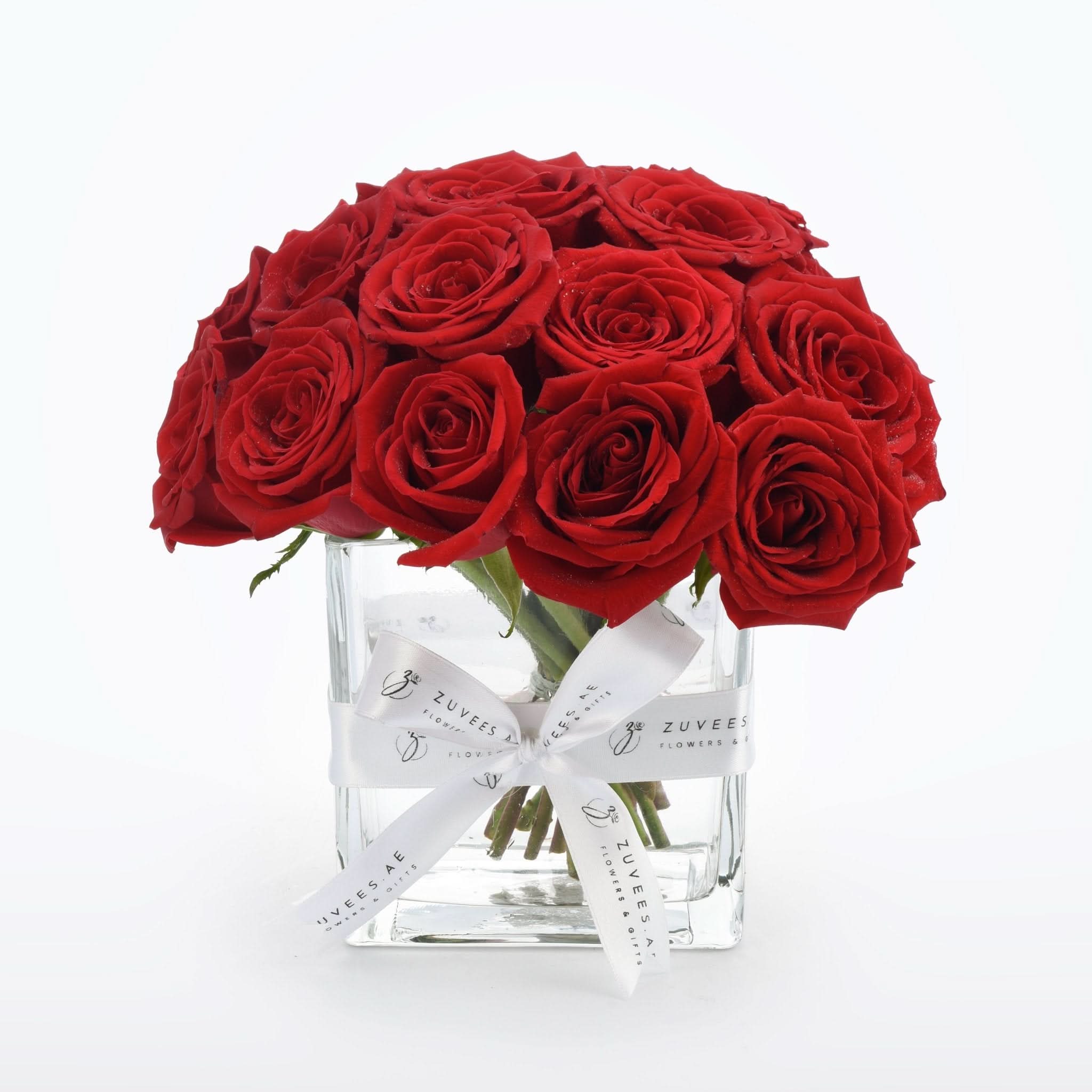 Vibrant red roses in clear glass vase, elegantly tied with branded white ribbon.