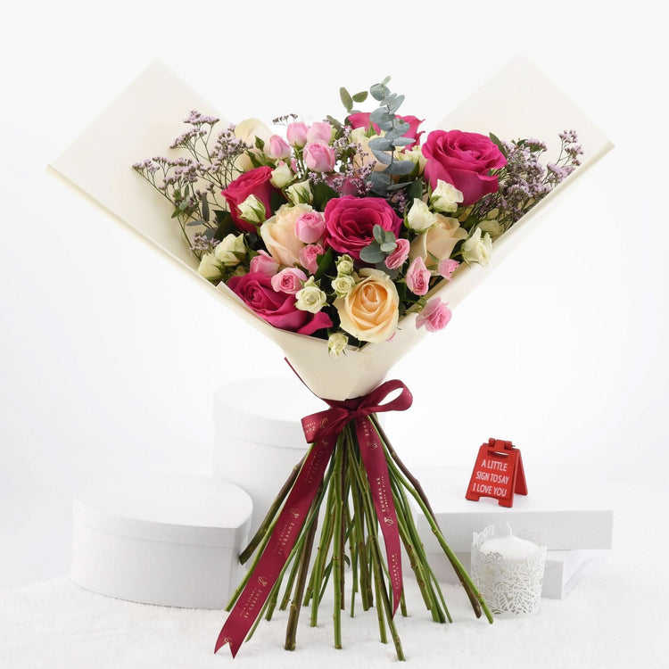 Vibrant pink, peach, and white roses wrapped in cream paper with burgundy ribbon.