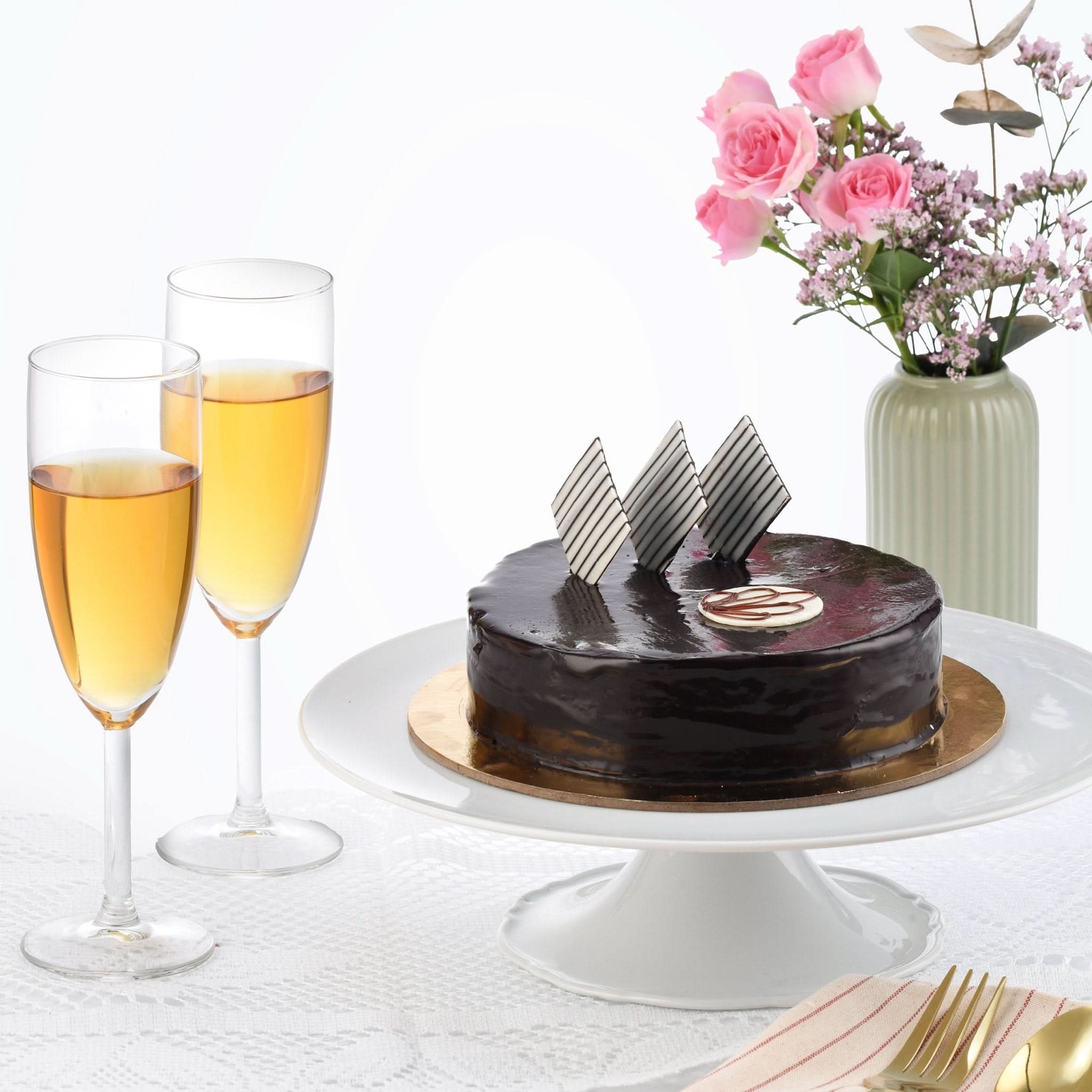 Glossy chocolate cake with striped chocolate shards, champagne flutes, and pink roses.