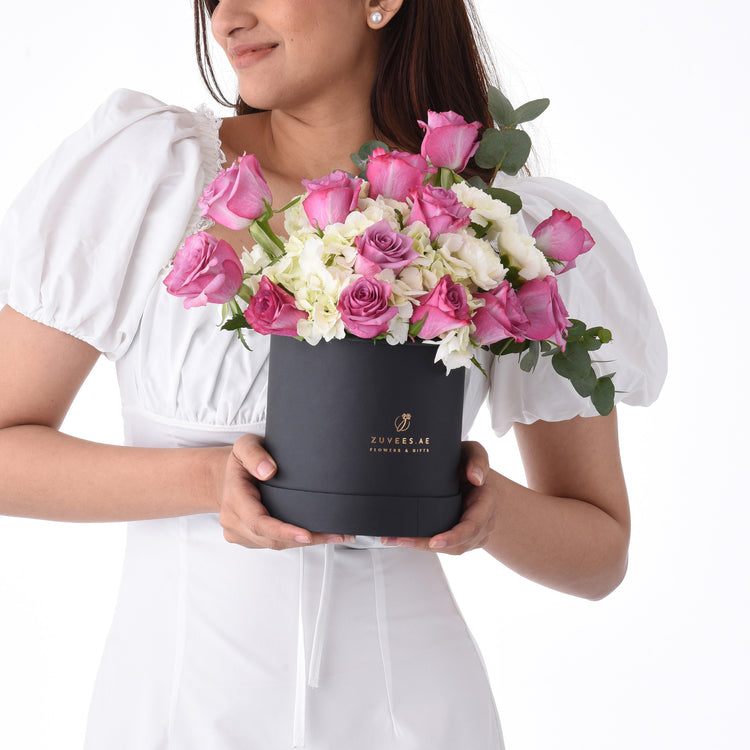 Elegant woman holds black box filled with pink roses and white hydrangeas.
