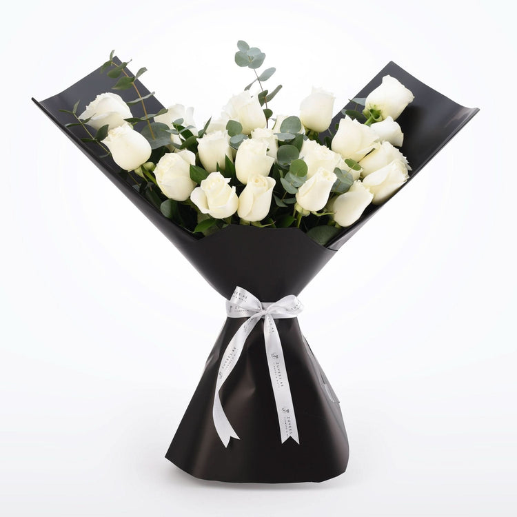 Elegant white roses wrapped in matte black paper with silver ribbon bow.