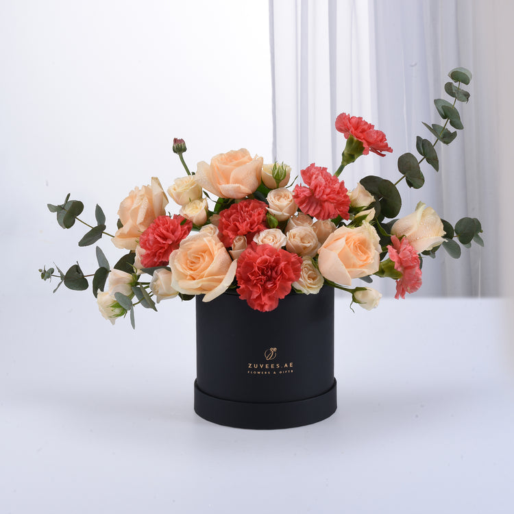 Elegant peach roses, coral carnations, and eucalyptus in a sleek black Zuvees box.