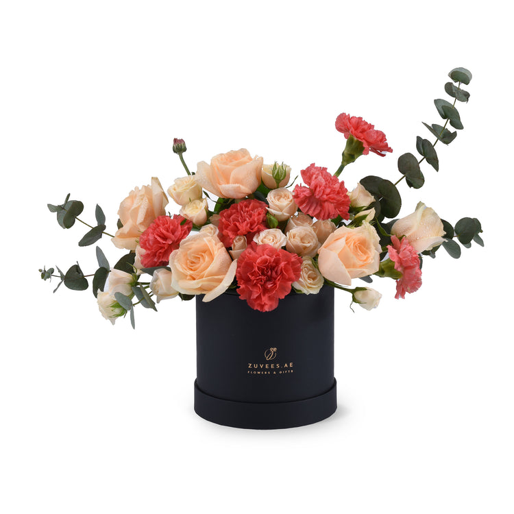 Elegant peach roses and red carnations in sleek black box with eucalyptus.